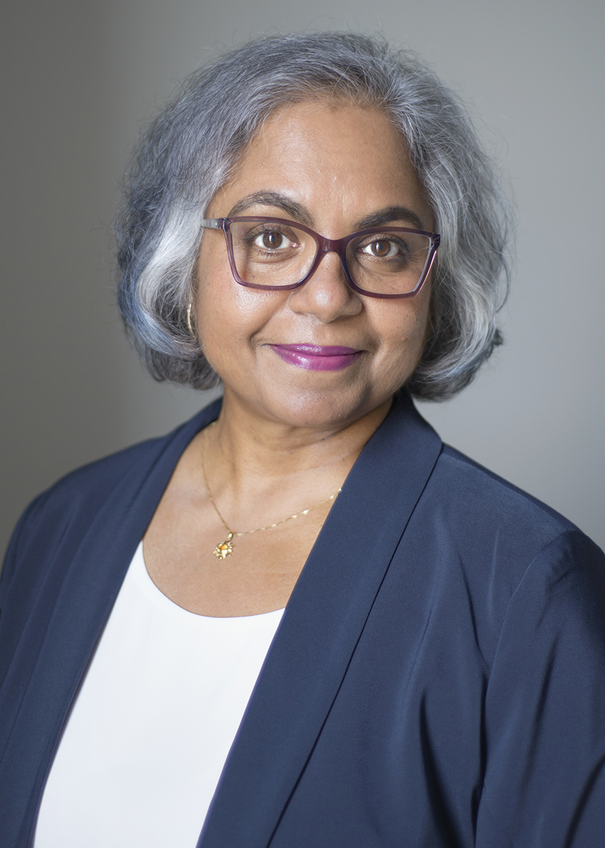 Coach Elizabeth Hesp smiling with black and white hair and wearing navy jacket and white top with purple glasses.